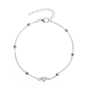 Flat lay of a silver bead chain anklet with a heart pendant and lobster clasp detail
