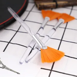 Detailed view of three fan-shaped facial mask brushes with orange bristles and acrylic handles