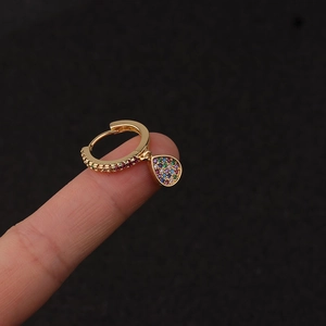 Close-up of golden hoop earring with colorful zircon teardrop pendant held on finger