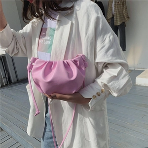 Pink pleated dumpling crossbody bag shown on model in natural outdoor setting