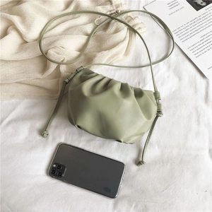 Detail of sage green pleated cloud bag with slim crossbody strap on white fabric