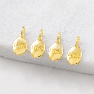 Four golden LOVE oval pendants with connectors on elegant white marble surface