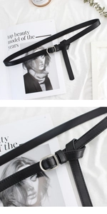 Detail of a thin black leather belt featuring a polished silver square D-ring metal buckle