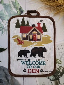 Close-up of a thick cotton potholder with bear and forest print on white wood background