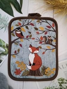 Detail of forest animal oven mat with hanging loop on a rustic white wooden background