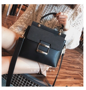Detail of black structured crossbody bag with gold square buckle and wide strap