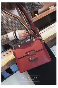 Detailed view of the dark red leather crossbody bag with a gold buckle worn by a model