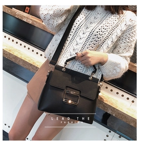 Close-up of a matte black mini bag featuring a prominent wide-rimmed golden square buckle