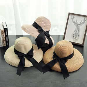 Three straw sun hats with black ribbon bows in cream, beige and khaki on a dark table