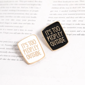 Black and white enamel lapel pins with It's Too Peopley Outside text on book