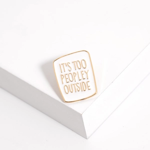 Detailed shot of enamel brooch with slogan It's Too Peopley Outside on white stand