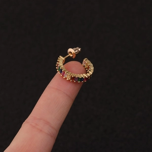 Close-up of golden C-shaped earring with colorful zircon stones held on a finger
