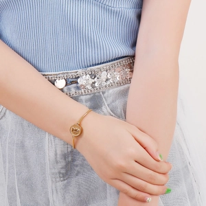 Detail of gold coin bracelet with rose embossed charm on woman wrist