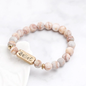 Macro detail of natural stone beaded bracelet featuring a gold plate engraved with Belief