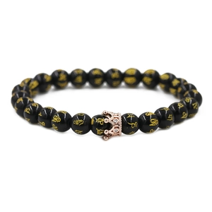 Detail of black beads with golden mantras and a rose gold crown charm on a bracelet