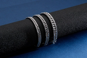 Three width options of silver Cuban link bracelets displayed on a sleek black cylinder stand