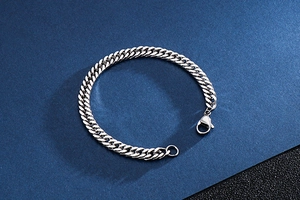 Close-up of a silver Cuban link chain bracelet with a lobster clasp on a blue surface