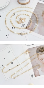 Detail of a gold-tone thin chain belt featuring white pearls and a metal bee charm