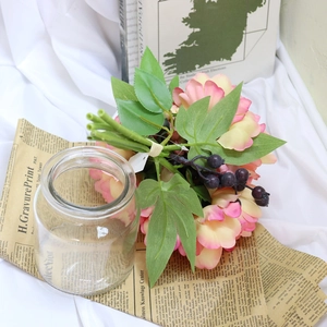 Pastel pink faux flowers and purple berries in glass jar on vintage paper background