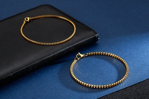 Close-up of dual gold stainless steel box chains on dark textured background