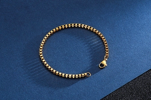 Detailed close-up of golden stainless steel box chain bracelet with lobster clasp finish