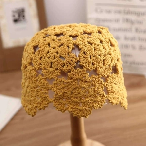 Yellow hand-crocheted hollow floral knit beanie cap on a wooden model head
