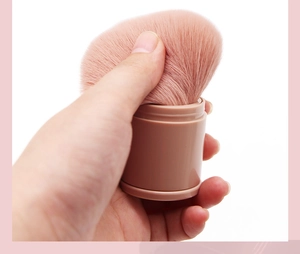 Close-up of hand pressing soft pink bristles of the retractable powder makeup brush