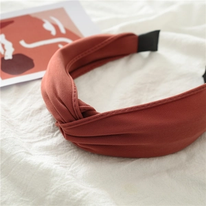 Close-up of a wide reddish-brown knotted fabric headband on a textured white background