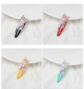 Detail showing four colored cat-print hair clips on white ceramic and linen background