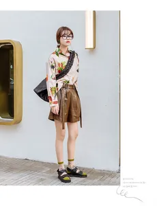 Detailed view of beige long sleeve cotton shirt with realistic fruit print and leather shorts