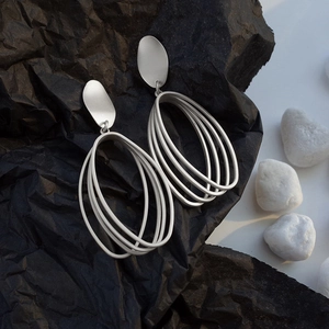 Minimalist matte silver geometric oval dangle earrings on textured black background