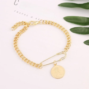 Close-up of golden chain bracelet with retro coin pendant and safety pin charm