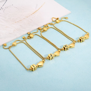 Adjustable gold heart charm bracelet with alphabet cubes on a light blue background
