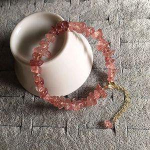 Detailed shot of pink strawberry quartz bracelet with gold clasp on a white ceramic bowl