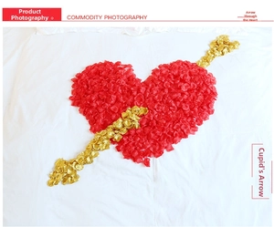 Romantic heart and arrow design made of red and gold artificial rose petals on a bed