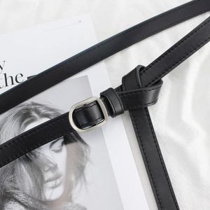 Minimalist black leather skinny belt with a silver D-ring buckle on a textured background