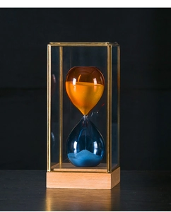 Close-up of a luxury two-tone glass hourglass inside a gold-edged case with a wood base