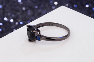 Macro shot of S925 engraved black metal band with heart-cut black stone and blue gems