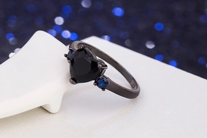 Close-up of black heart-shaped ring with blue stones on a white ceramic display