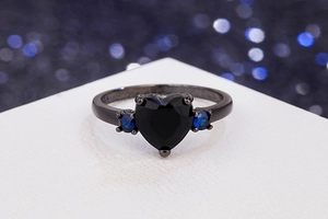 Macro shot of gun black heart ring with black gem and blue side stones on white stand