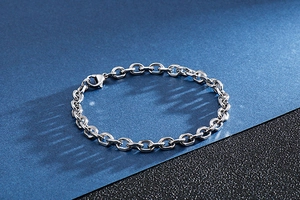 Detail of silver stainless steel curb chain bracelet on a textured dark background