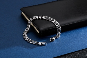 Detail of silver Cuban link chain bracelet with lobster clasp on a black journal
