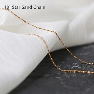 Detailed macro shot of a golden star sand chain necklace on silk and stone backdrop