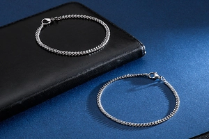 Close-up of two silver Cuban link bracelets on textured leather and navy backgrounds