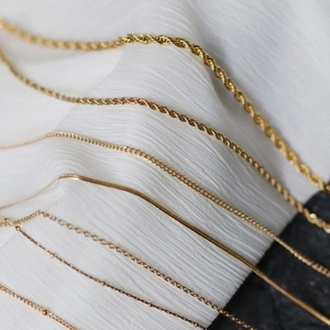 Assorted gold plated stainless steel twist and snake chains on white fabric background