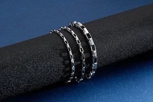 Close-up of three polished stainless steel box chain bracelets in various thicknesses