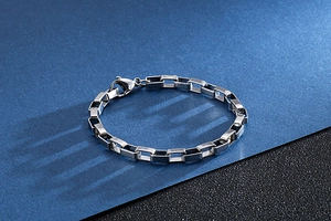 Macro detail of silver stainless steel box chain bracelet featuring a secure lobster clasp