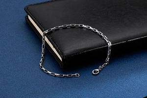 Detail of silver stainless steel grid chain bracelet with lobster clasp on leather background