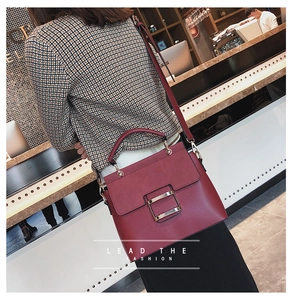 Detail view of burgundy matte leather crossbody bag with square metal buckle on model