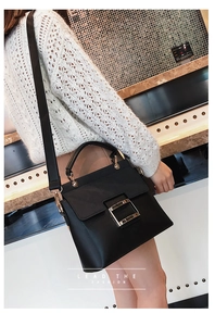 Close-up of matte black crossbody bag with golden buckle and wide strap on model